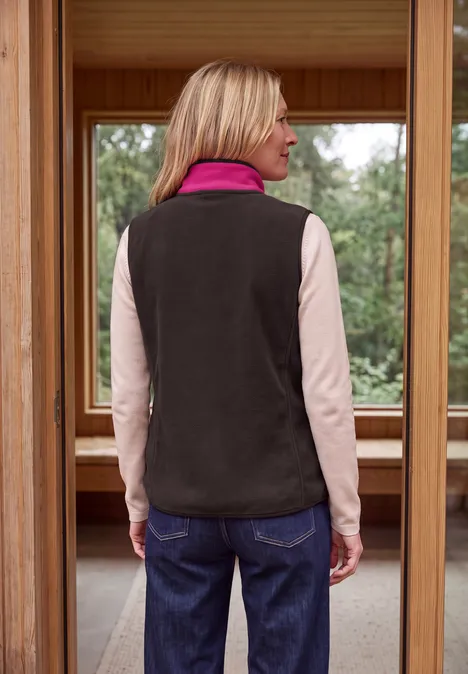 Frau von hinten in rosa Langarmshirt, grauer Fleeceweste und Jeans, stehend in Holzrahmen.