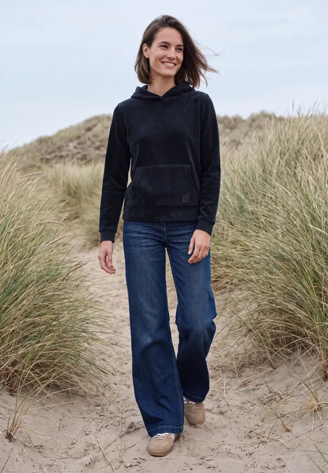 Langarm Shirt aus Cord mit Kapuze urban dark blue Frau in lässigem Hoodie und Jeans steht lächelnd in Dünen mit Strandgras.
