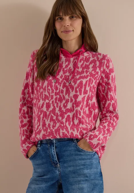 Langarm Shirt mit Fake-Kapuze pink flash Frau trägt pink-weiß gemusterten Kapuzenpullover und blaue Jeans vor hellem Hintergrund.