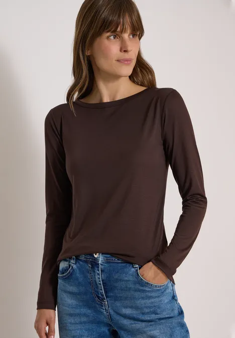 Langarm Shirt in Unifarbe mit Boat Neck truffle brown Junge Frau mit braunem Langarmshirt und Jeans, entspannt stehend und seitlich blickend vor hellem Hintergrund.