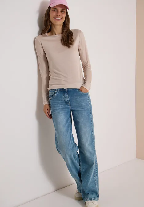 Langarm Shirt in Unifarbe mit Boat Neck cashmere beige Frau in beige Langarmshirt, blauen Jeans und rosa Cap lehnt lächelnd an der Wand.