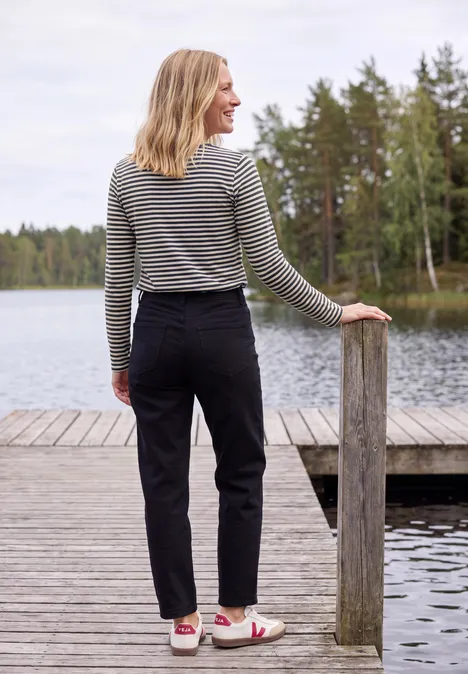 Langarm Shirt mit Boat Neck und Streifen urban dark blue Frau in gestreiftem Pullover und schwarzer Hose steht auf einem Steg am See und blickt aufs Wasser.