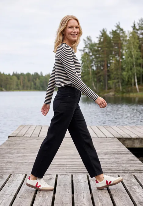 Langarm Shirt mit Boat Neck und Streifen urban dark blue Eine fröhliche Frau in gestreiftem Shirt und schwarzen Hosen geht auf einem Holzsteg an einem See entlang.