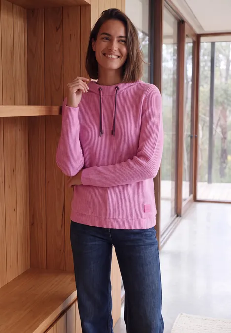 Shirt in Rippstruktur mit Funnel Neck pink flash melange Lächelnde Frau in rosa Kapuzenpullover und Jeans steht in modernem Raum am Fenster.