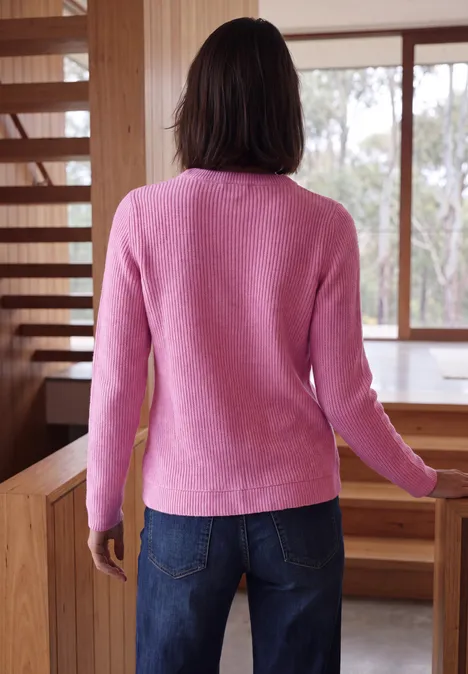 Shirt in Rippstruktur mit Funnel Neck pink flash melange Frau von hinten in pinkem Pullover und Jeans, die in einem Raum mit Holzmöbeln steht.