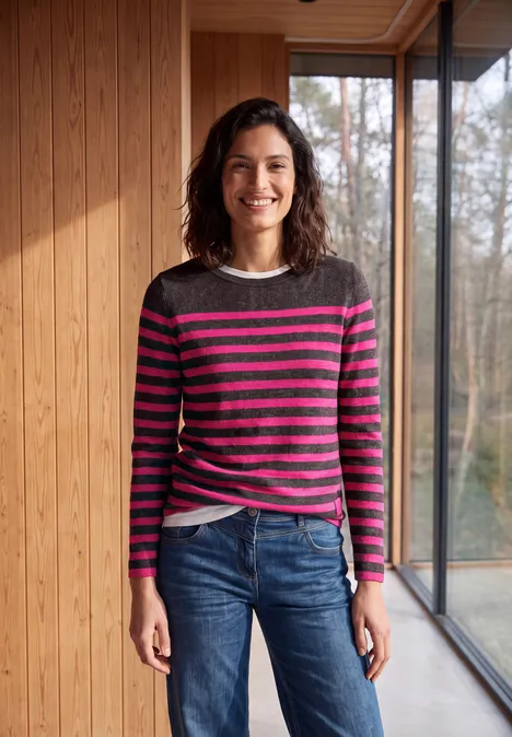 Vrouw lacht in een modern houten interieur, draagt een gestreepte trui en spijkerbroek.