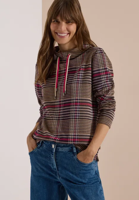 Langarm Shirt mit Funnel Neck und Muster dark toffee brown Lächelnde Frau in kariertem Hoodie mit pinken Streifen und blauen Jeans, Hände in den Taschen.
