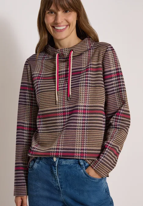 Langarm Shirt mit Funnel Neck und Muster dark toffee brown Lächelnde Frau im karierten Braun-Pink-Hoodie und blauen Jeans vor weißem Hintergrund.