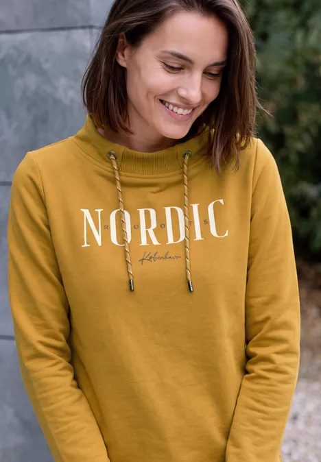 T-shirt à manches longues avec col cheminée et inscription golden honey Junge Frau in senfgelbem Hoodie mit Aufschrift 'NORDIC', lächelnd und nach unten blickend.