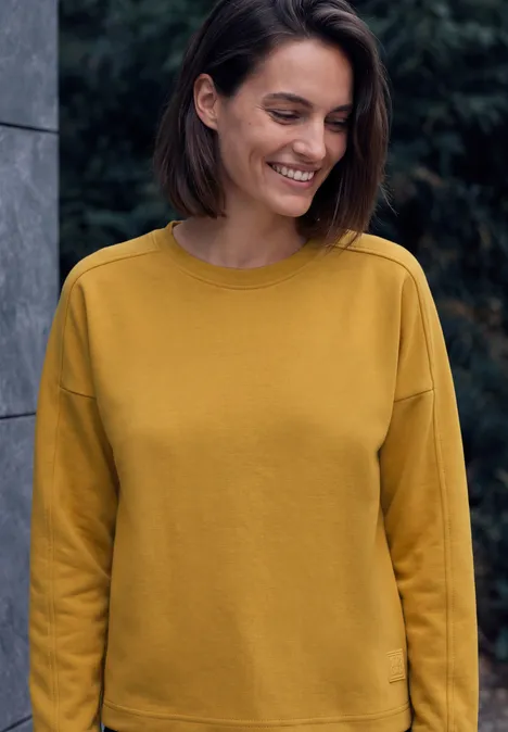 Shirt met lange mouwen, ronde hals en geribbelde structuur golden honey Fröhliche Frau mit kurzem dunklem Haar trägt einen senfgelben Pullover und lächelt leicht.