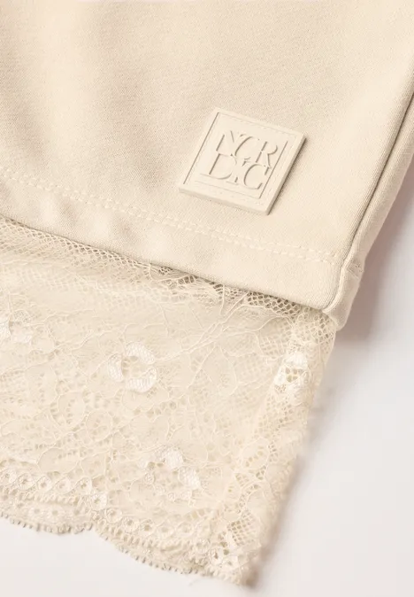Nahaufnahme eines beigen Tops mit feiner Spitzenkante und eckigem Labeldetail.