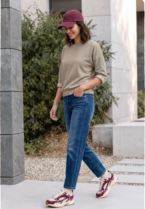 Shirt met lange mouwen en visgraatpatroon pearl beige Jonge vrouw in spijkerbroek, trui, rode pet en sneakers wandelt buiten en lacht.