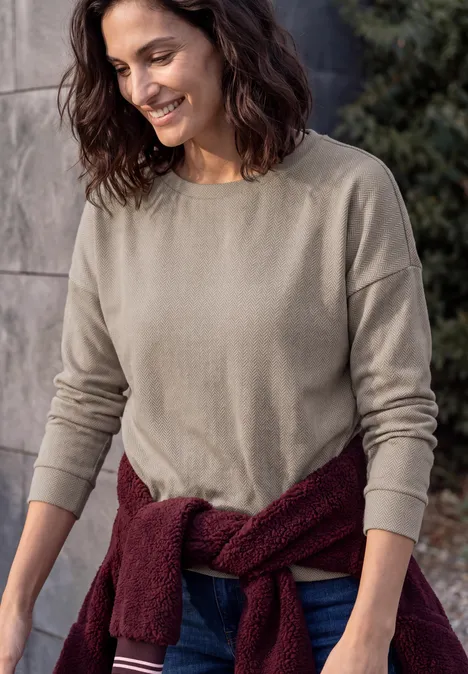 Shirt met lange mouwen en visgraatpatroon pearl beige Glimlachende vrouw in beige shirt met lange mouwen, bordeaux trui om de taille gestrikt, voor een stenen muur.