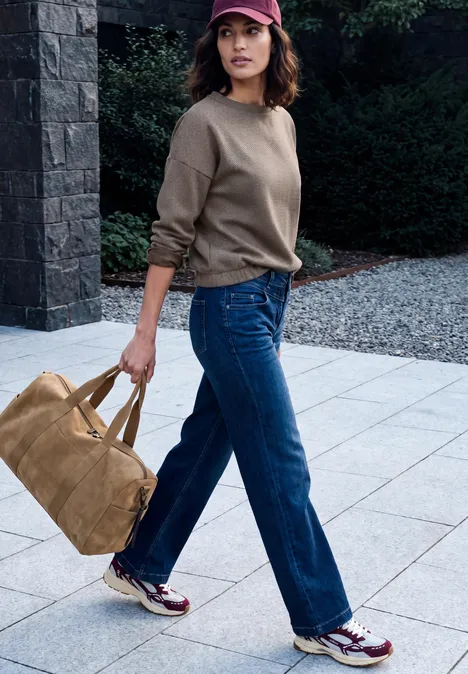 Langarm Shirt mit Herringbone-Muster truffle brown Frau in Freizeitkleidung mit Jeans, Pullover und Tasche schlendert auf gepflastertem Weg.