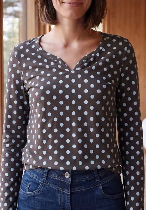 Eine Person trägt ein braunes Langarmshirt mit weißen Punkten und eine blaue Jeans.
