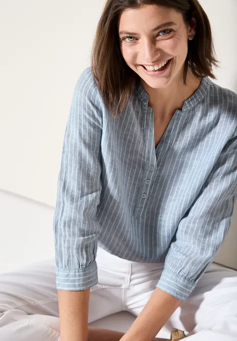 Lachende vrouw met blauw gestreepte blouse en witte broek.