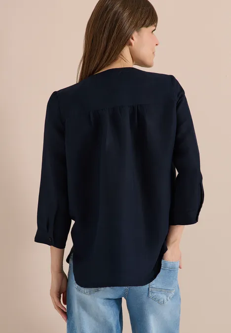 Eine Frau von hinten, trägt eine dunkelblaue Bluse und helle Jeanshose.