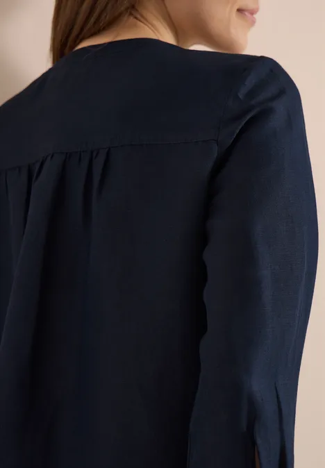 Rückenansicht einer Frau in einer dunkelblauen Bluse, leichte Rückenfalte, Schulterausschnitt sichtbar.
