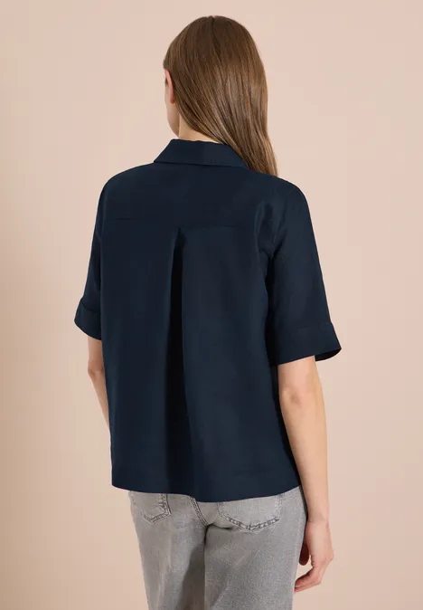 Rückansicht eines Modells in dunkelblauem Kurzarmhemd und grauer Jeans.