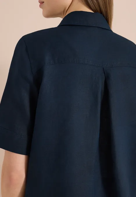 Rückansicht einer Person in einer dunkelblauen, kurzärmeligen Hemdbluse mit Rückenfalte.