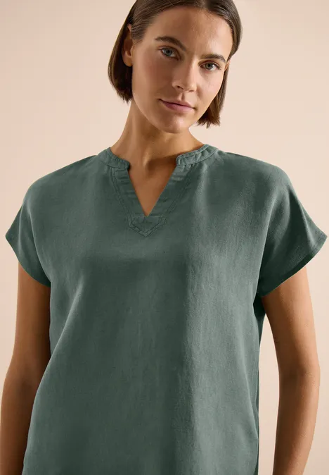 Frau trägt dunkelgrünes, kurzärmeliges Oberteil mit V-Ausschnitt.