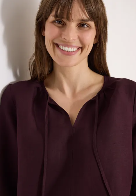 Frau mit weinrotem Oberteil, verschwommenem Gesicht und offenem Haar, Schulteransicht vor hellem Hintergrund.