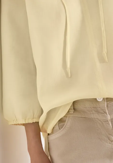 Nahaufnahme einer Person in gelbem Pullover mit Kordelzug und beigen Hosen.