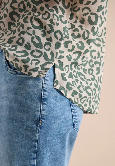 Detailaufnahme einer grünen Leopardenmuster-Bluse und blauer Jeanshose.