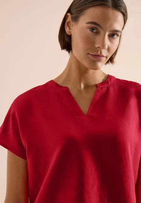 Frau mit roter Bluse und V-Ausschnitt vor neutralem Hintergrund