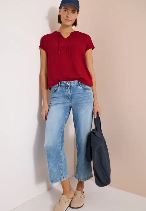 Frau in roter Bluse, weiten hellblauen Jeans und beigen Schuhen trägt eine dunkelblaue Tasche.