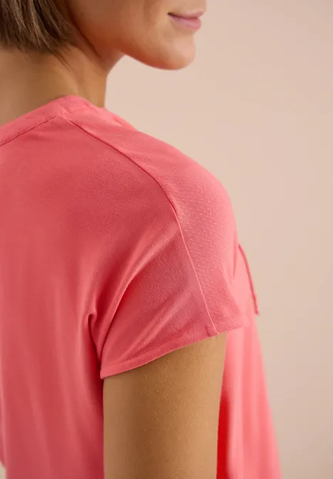 Nahaufnahme einer Frau in einem korallfarbenen T-Shirt, Fokus auf Schulter und Ärmeldetail.