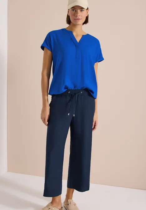 Frau in einer kobaltblauen Bluse mit V-Ausschnitt und dunkelblauer Culotte-Hose.