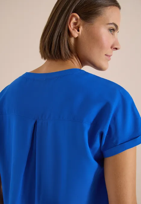 Frau von hinten mit schulterlangem Haar trägt ein kurzärmeliges, knallblaues Oberteil.