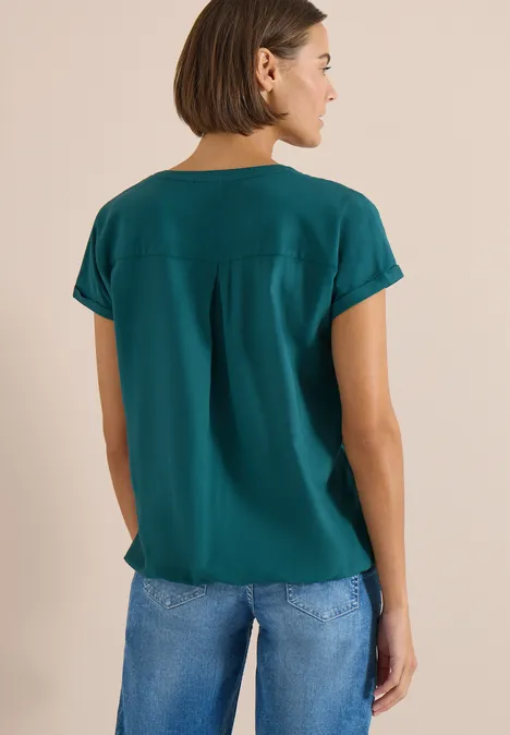 Een vrouw van achteren in een groen t-shirt en een blauwe spijkerbroek.