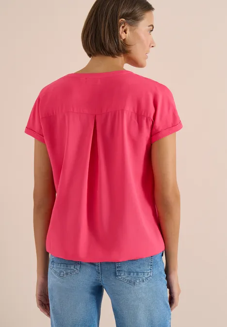 Vrouw van achteren in een felroze blouse met korte mouwen en spijkerbroek voor neutrale achtergrond.