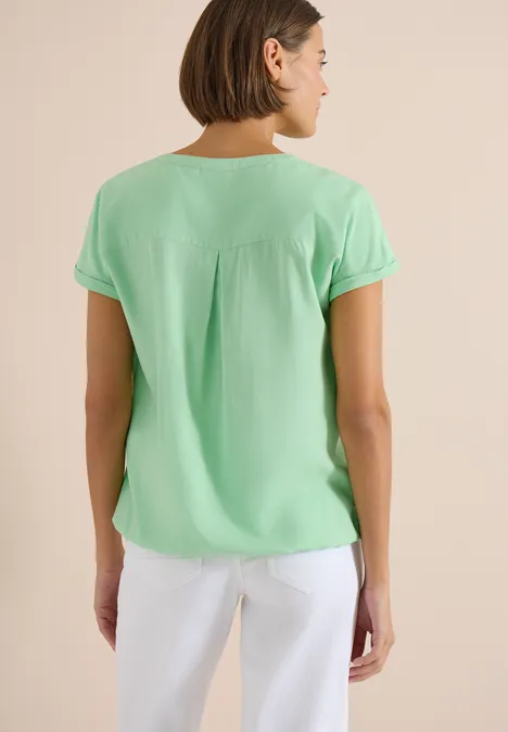 Vrouw van achteren in mintgroene blouse met korte mouwen en witte broek.