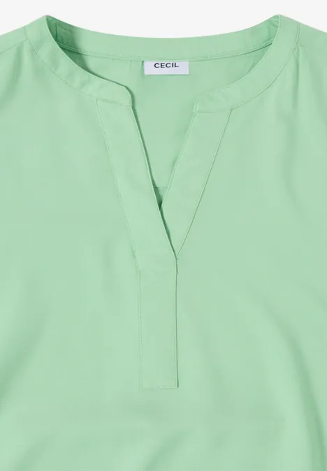 Lichtgroene damestop met V-hals en korte staanderkraag.