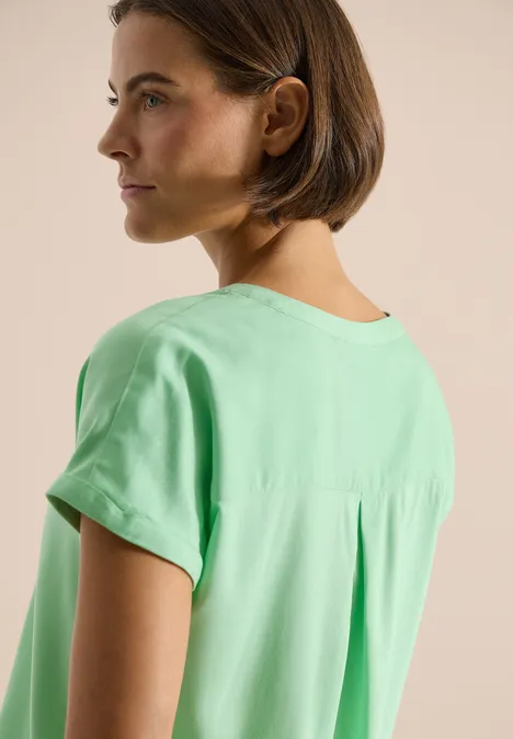Achteraanzicht van een persoon in een losse groene blouse met korte mouwen.