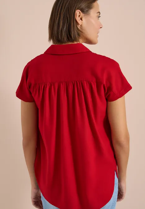 Femme vue de dos portant un chemisier rouge à manches courtes froncé dans le dos.