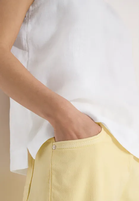 Weißes ärmelloses Top und gelbe Hose, Hand in Hosentasche.