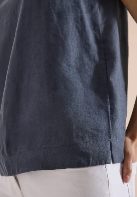 Gros plan sur un haut bleu marine avec fente latérale, porté avec un pantalon clair et main visible.