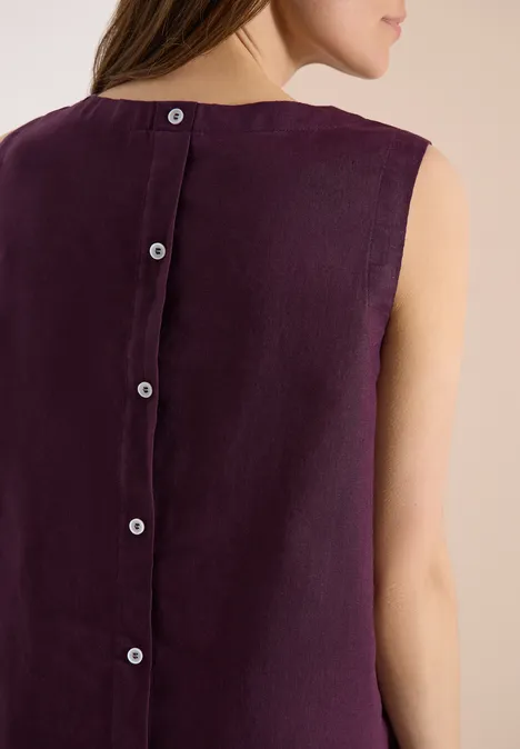 Frau von hinten in ärmellosem pflaumenfarbenem Leinentop mit Knopfleiste am Rücken.