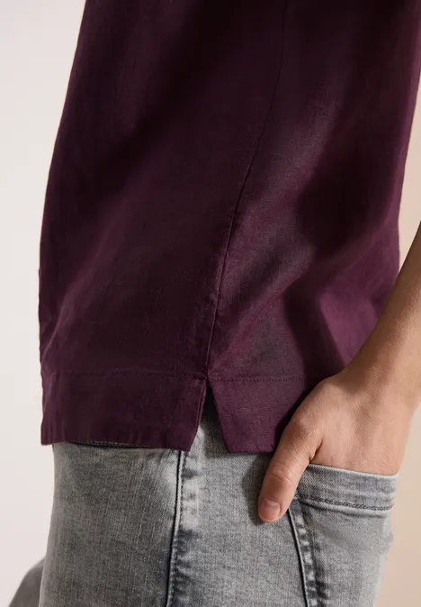 Ein Mensch trägt ein lila T-Shirt und helle Jeans, Hand in der Hosentasche.