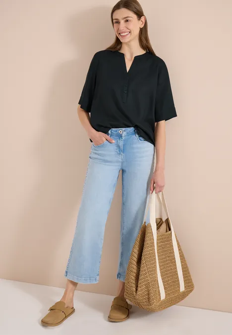 Frau trägt schwarzes Shirt, hellblaue Culotte-Jeans und Mokassins, hält großen geflochtenen Korb.