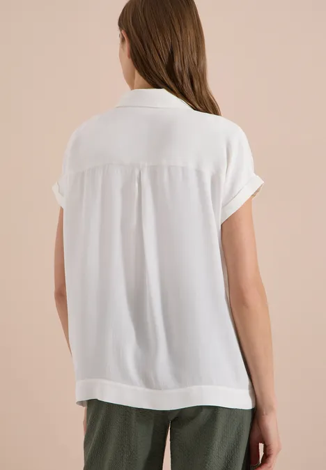 Chemisier à manches courtes uni vanilla white Femme vue de dos portant un chemisier blanc à manches courtes et un pantalon vert foncé sur fond neutre.