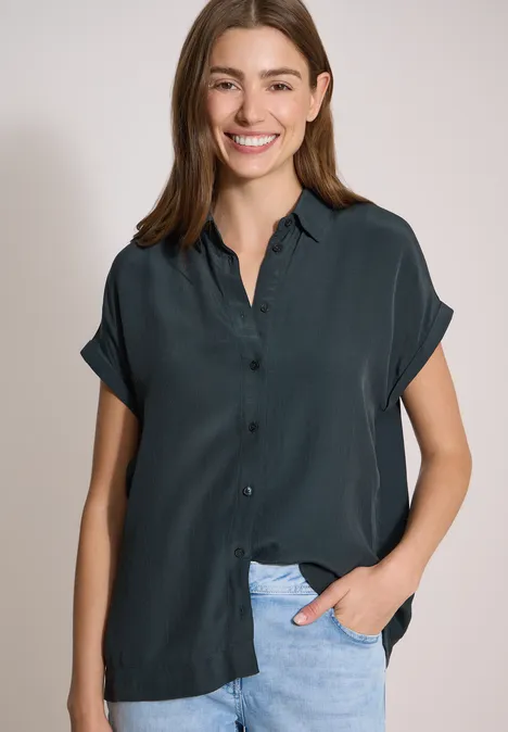 Chemisier à manches courtes uni palm breeze green Une femme porte une chemise bleu foncé à manches courtes et un jean clair.