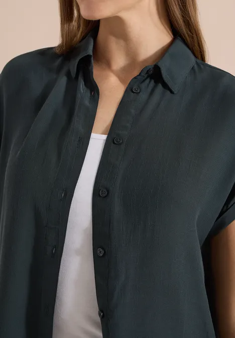 Chemisier à manches courtes uni palm breeze green Une personne porte une chemise sombre à manches courtes sur un débardeur blanc.