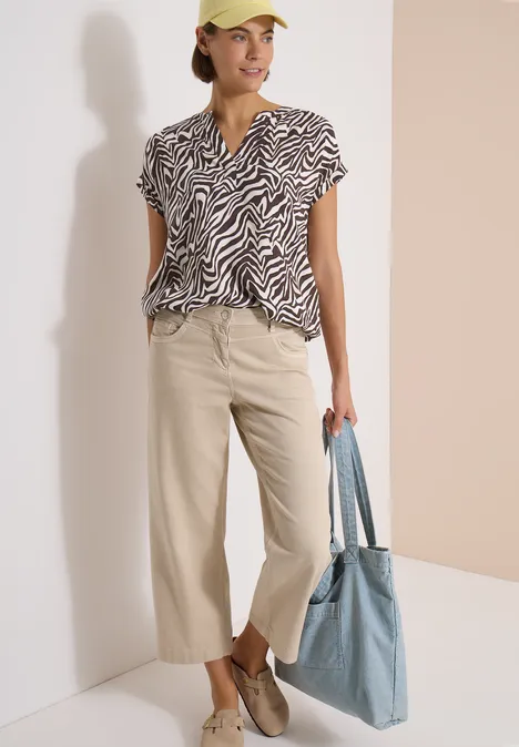 Femme en pantalon beige large, haut zébré, chaussures décontractées et tote bag bleu.