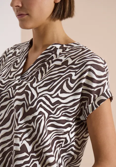 Une femme aux cheveux courts porte un chemisier à manches courtes au motif zèbre noir et blanc.