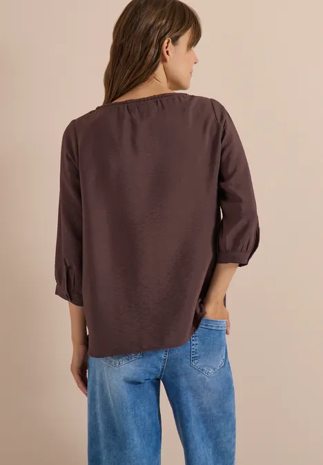 Frau von hinten in brauner Bluse und blauer Jeans.